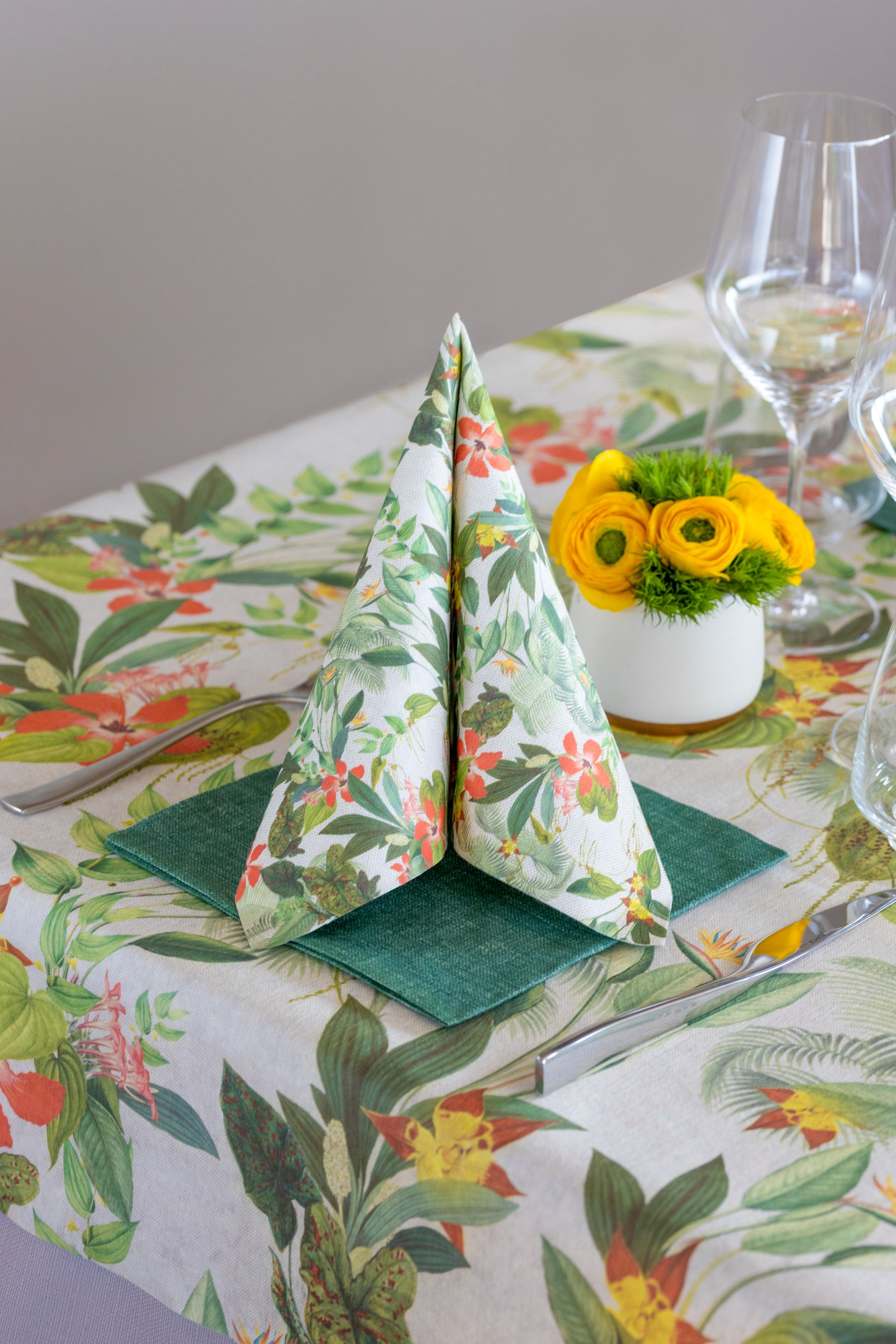 Serviette pliée en forme d'arbre sur une nappe fleurie, avec des fleurs et de la verrerie.