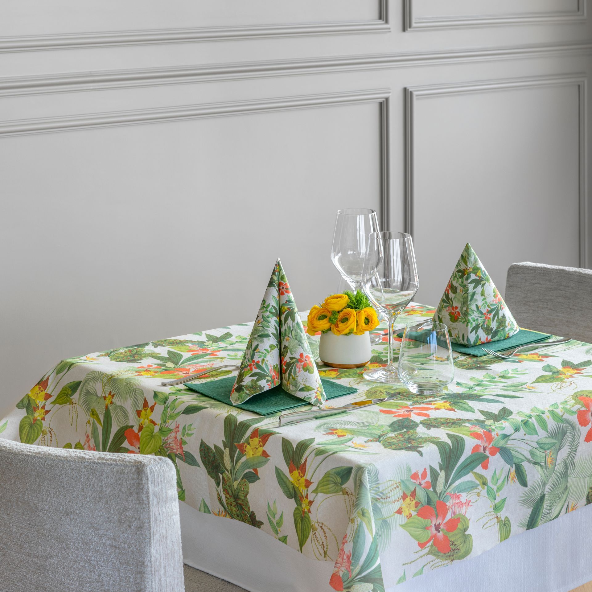 Une table dressée avec une nappe fleurie, des serviettes et des verres, avec une petite composition florale.