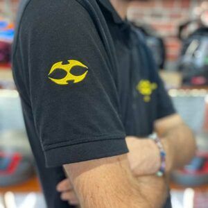 Homme portant un polo noir avec un logo jaune sur la manche.