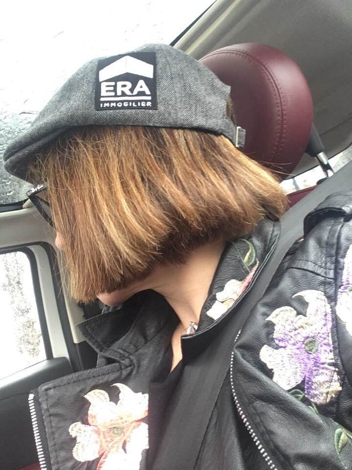 Personne dans une voiture portant un chapeau avec le logo ERA, regardant par la fenêtre, portant une veste noire avec broderie florale.