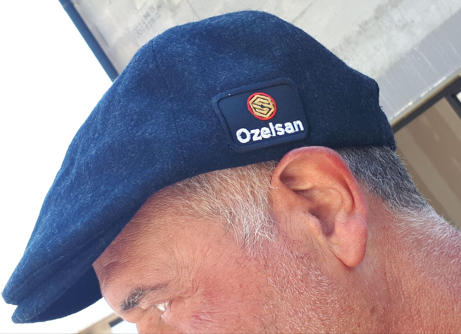 Homme portant un béret bleu foncé avec un logo « Ozelsan ».
