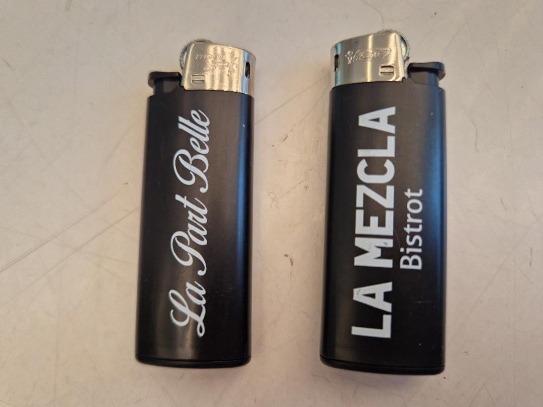 Deux briquets noirs avec inscription blanche. L'un porte l'inscription « La Part Belle », l'autre « LA MEZCLA Bistrot ».