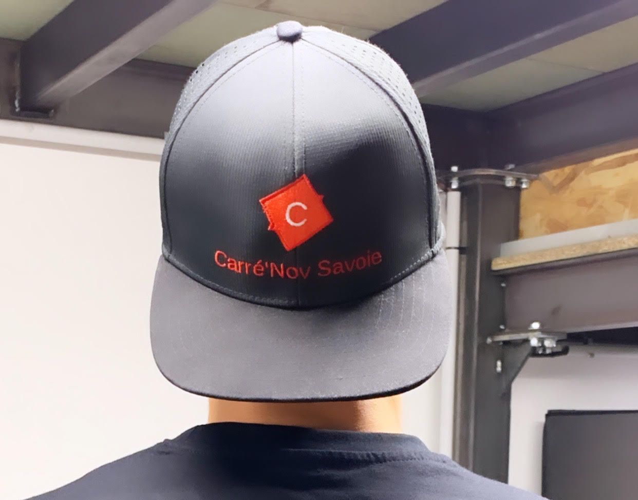 Personne portant une casquette gris foncé avec le logo « Carré'Nov Savoie » ; à l'intérieur.