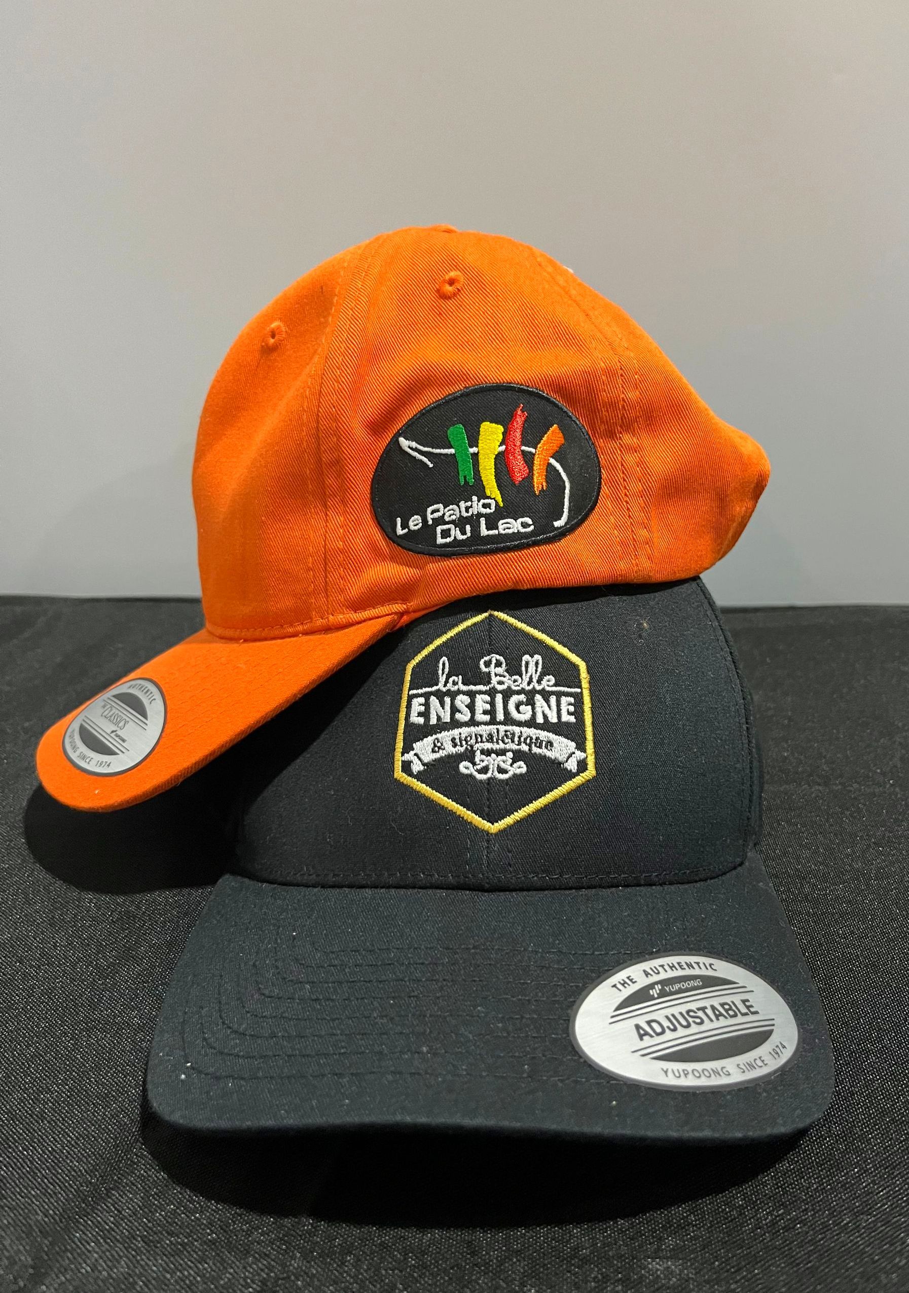 Deux casquettes de baseball empilées : orange sur le dessus avec un logo ; noire sur le dessous avec un patch.