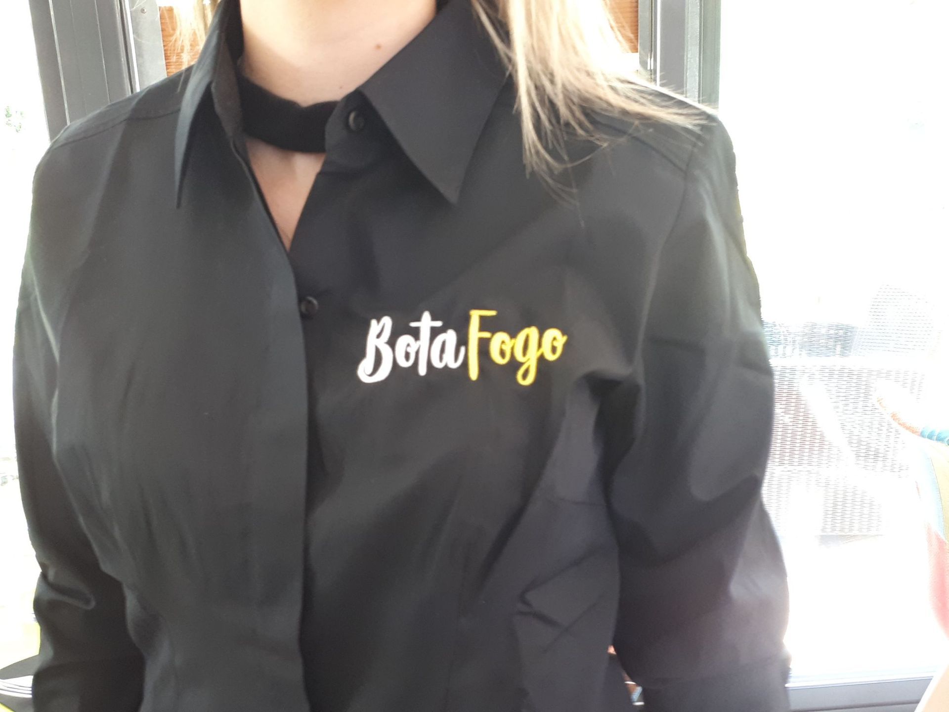 Femme portant une chemise noire avec le logo « Bota Fogo » en blanc et jaune.