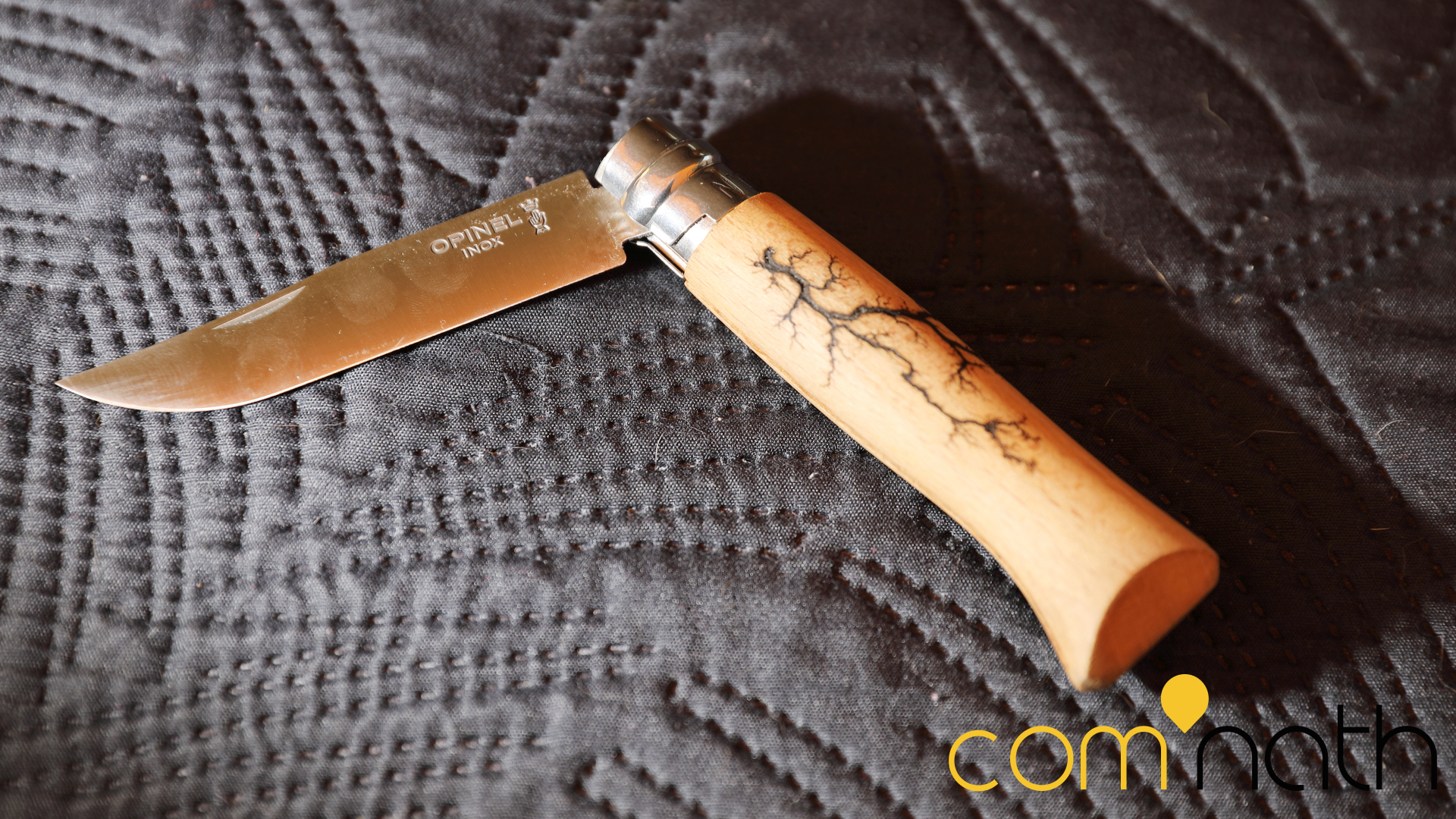 Un couteau pliant avec un manche en bois clair décoré d'un motif d'éclair sombre repose sur une surface sombre et texturée.