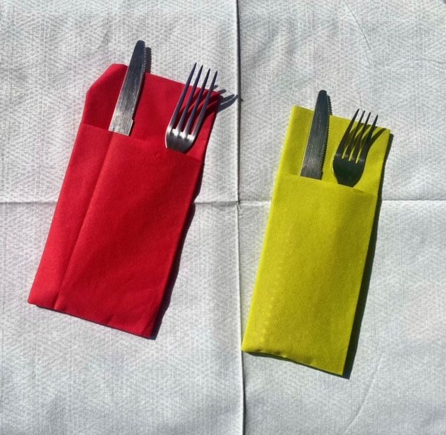 Deux ensembles d'argenterie emballés sur une nappe blanche : des paquets de papier rouge et jaune contiennent chacun un couteau et une fourchette.