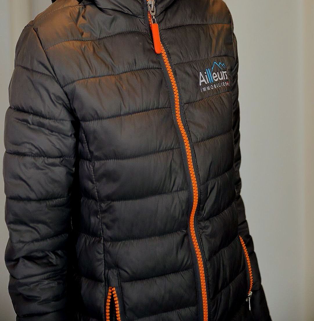 Doudoune noire avec détail de fermeture éclair orange et logo, personne la portant.