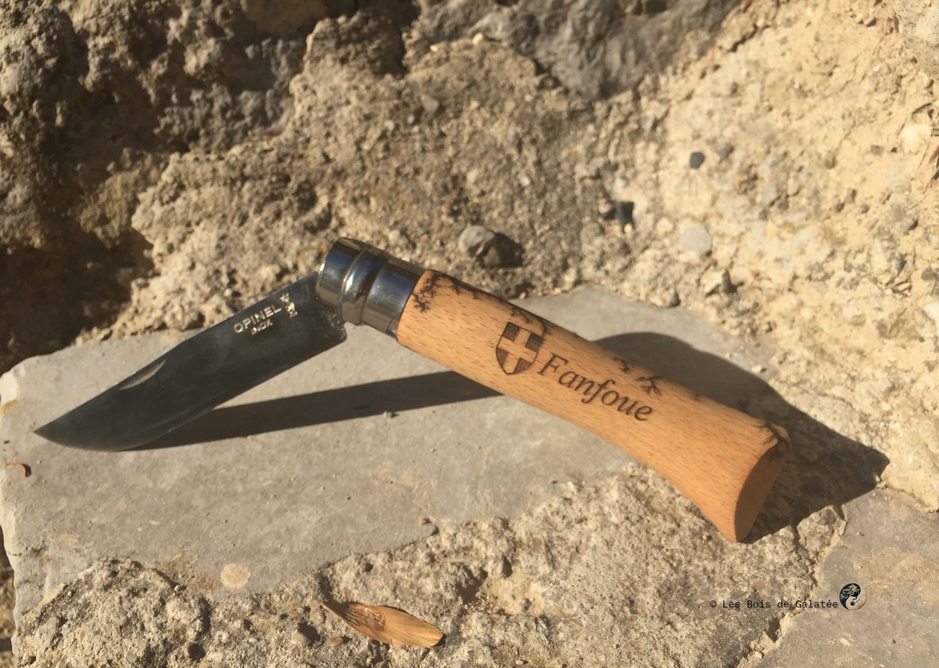 Couteau de poche avec manche en bois gravé; extérieur sur rocher, ombragé.