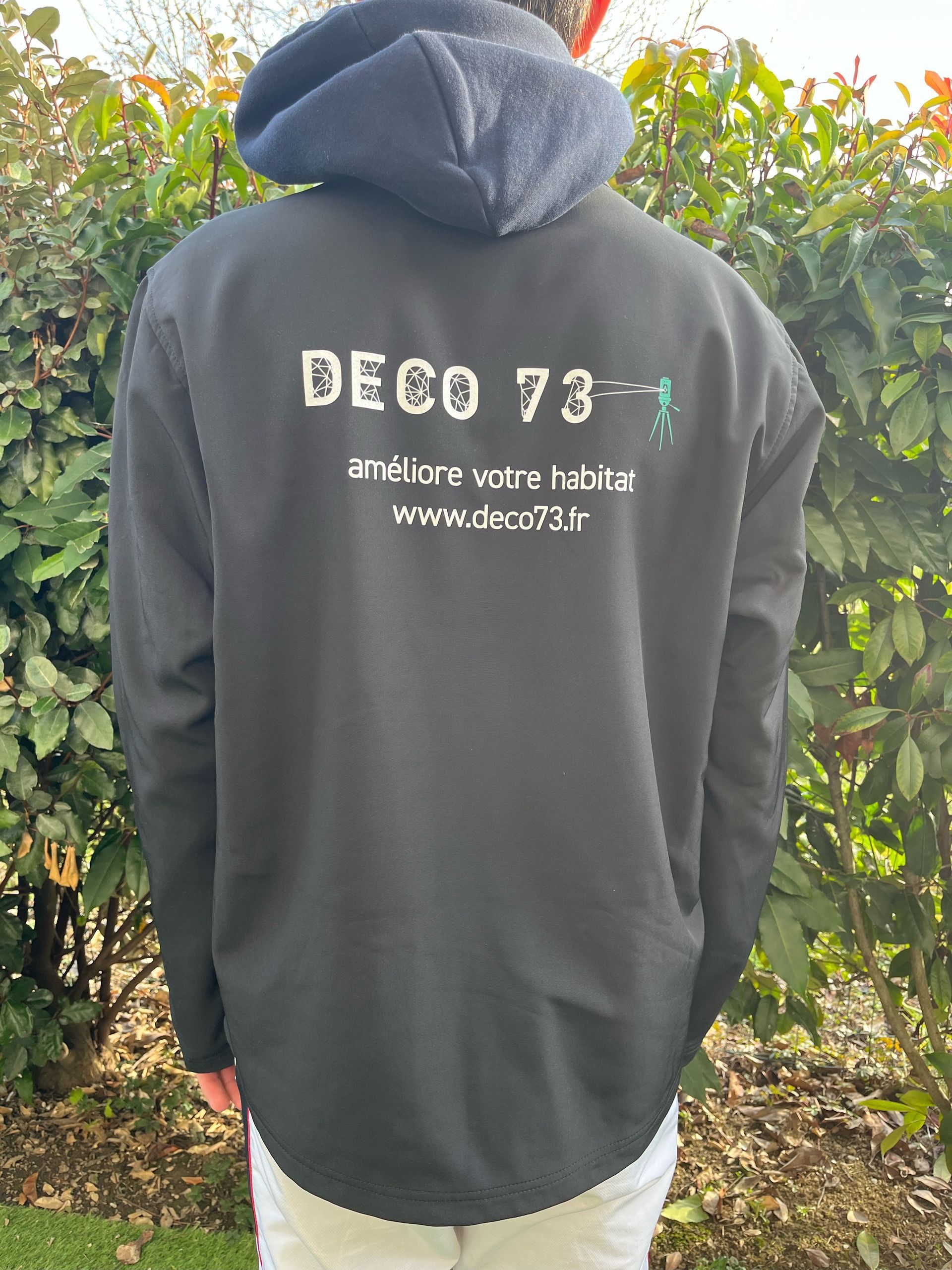 Personne portant un sweat à capuche noir avec le logo « DECO 73 » dans le dos, debout à l'extérieur.
