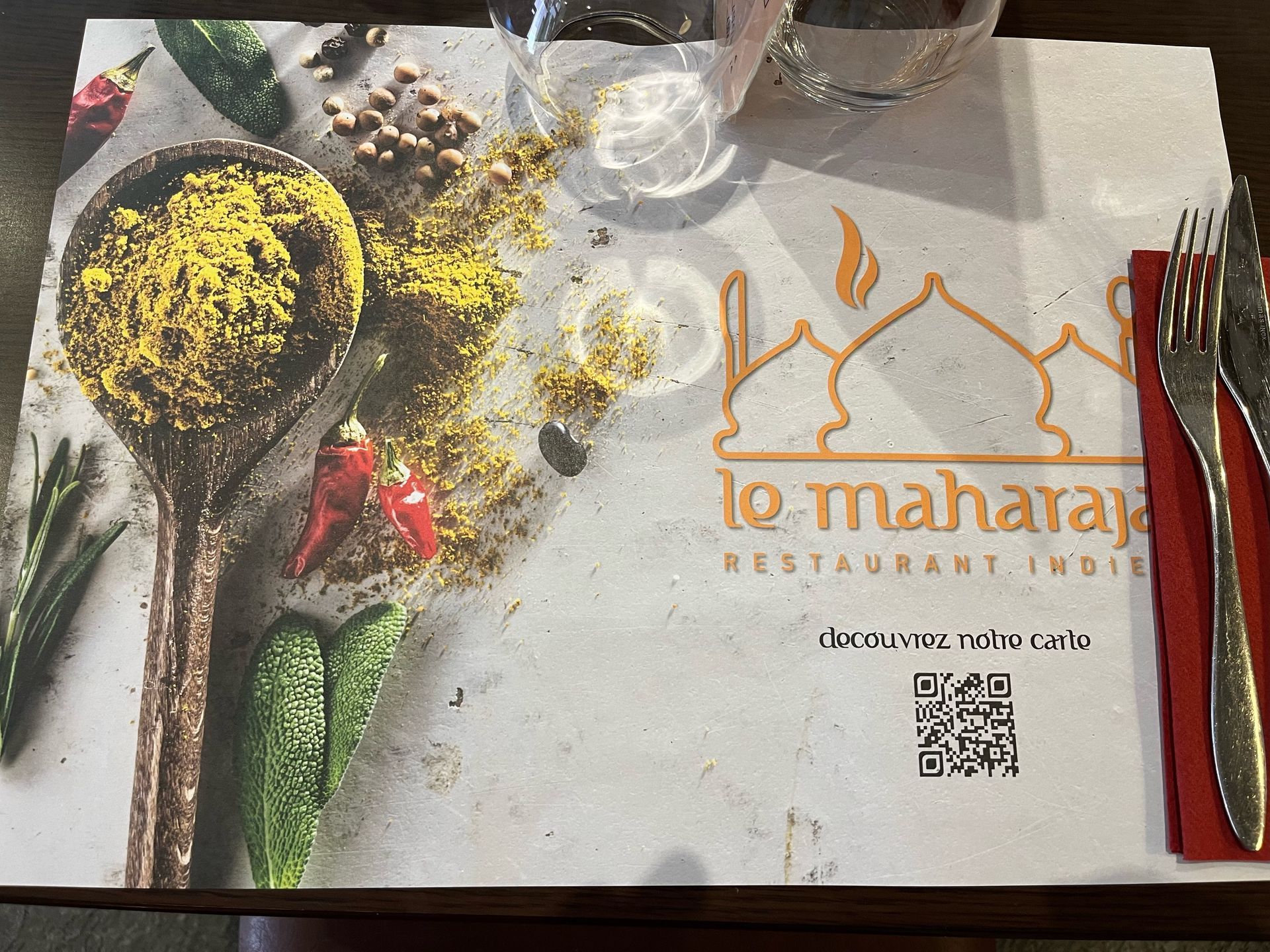 Set de table au restaurant « Le Maharaj, Inde » avec des épices, des couverts et un verre d'eau.