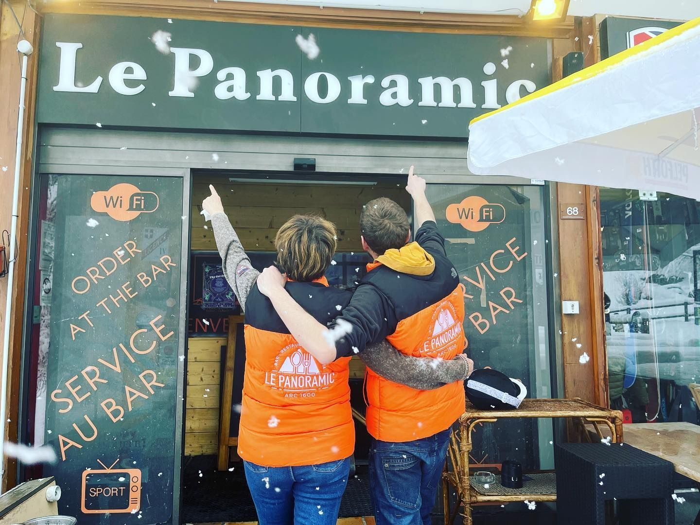 Deux personnes, les bras levés, font la fête devant le bar 