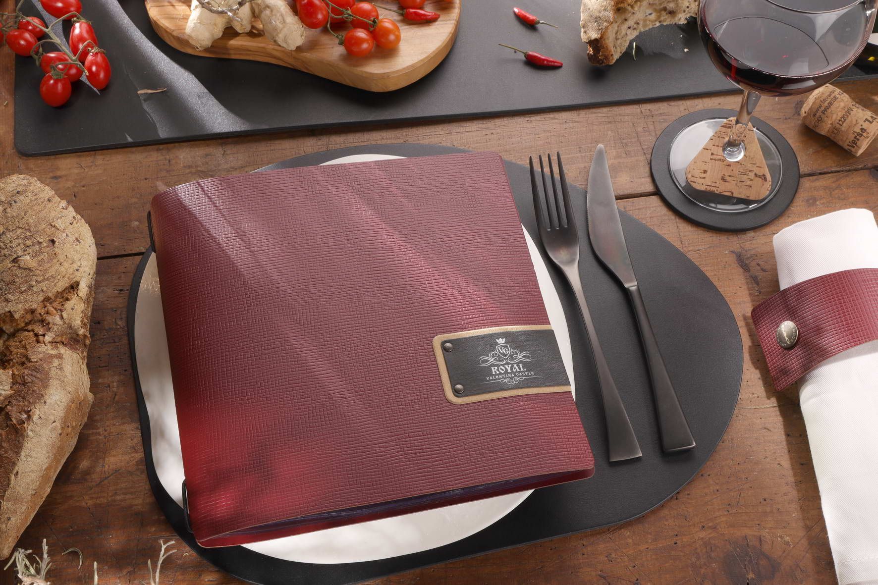 Gros plan d'une table de restaurant avec un menu rouge, des couverts, du pain et du vin.