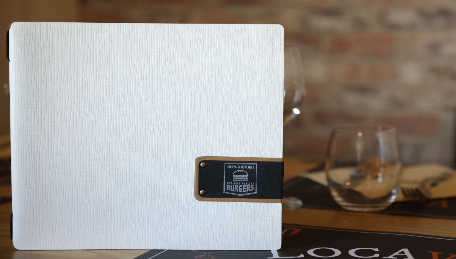 Menu blanc sur une table avec un petit panneau sombre ; verres et décor en arrière-plan.