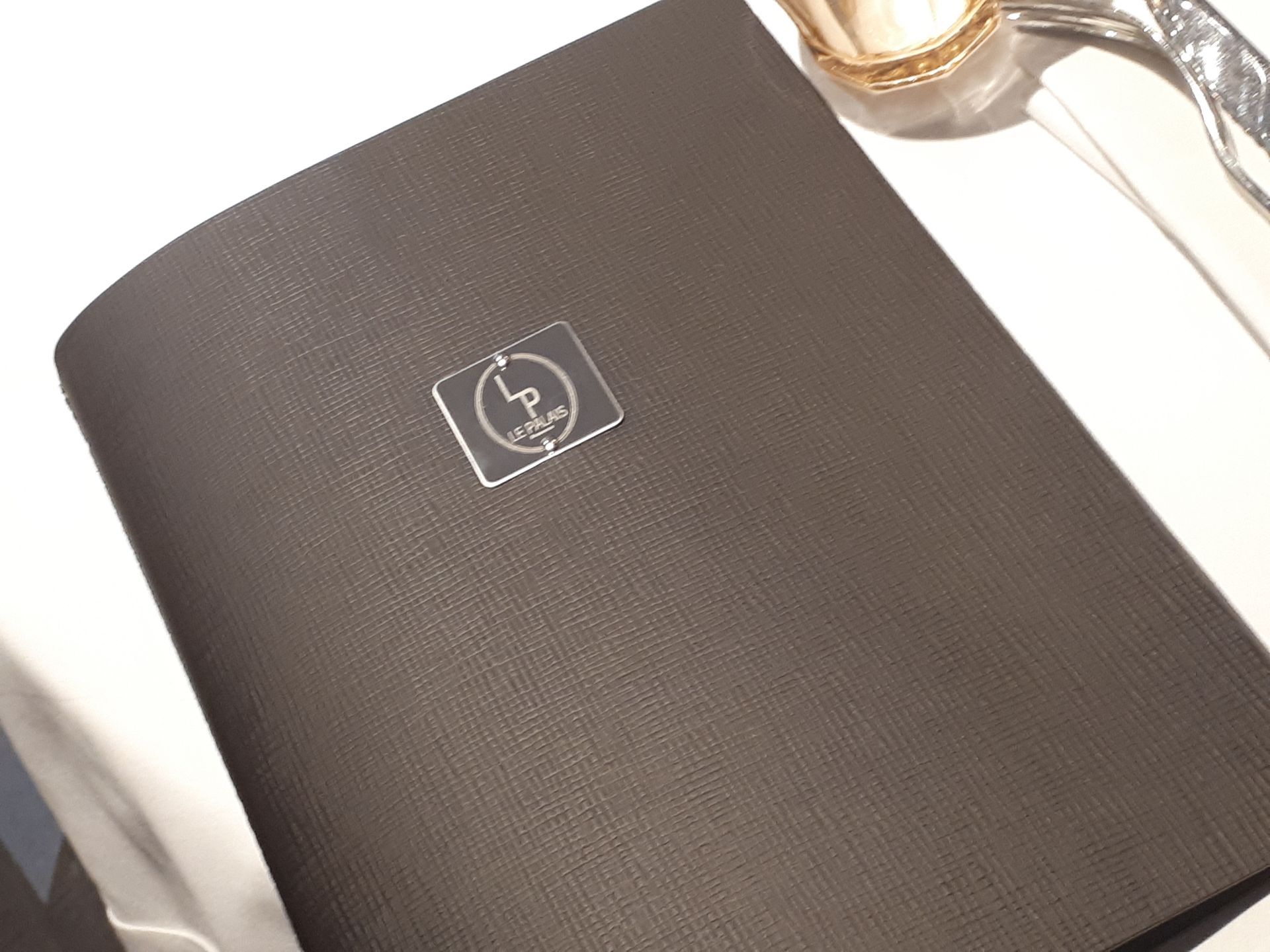 Chemise de menu marron foncé sur une nappe blanche avec logo argenté, service de table.