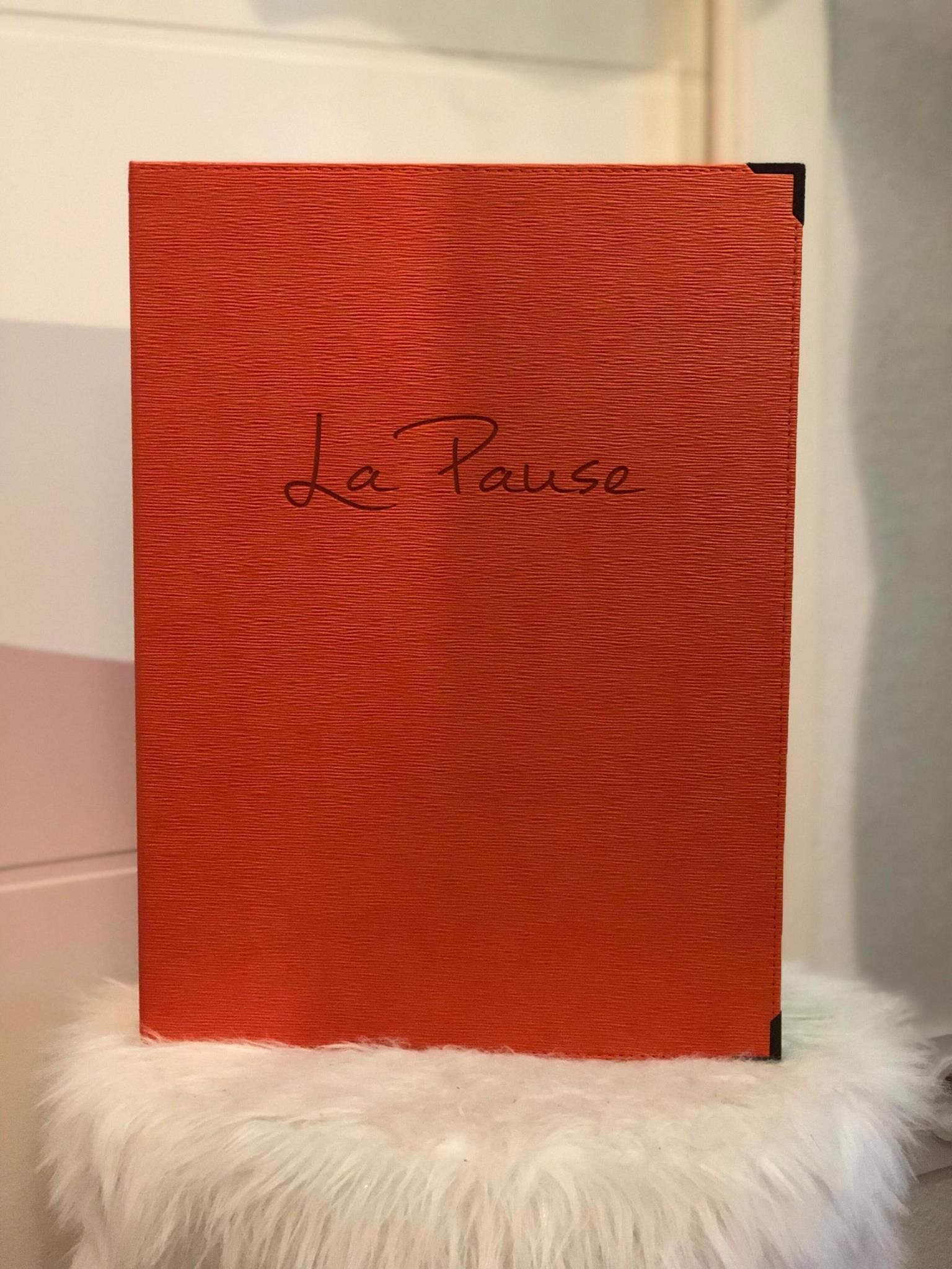 Classeur texturé rouge avec inscription « La Pause » en cursive sur un coussin blanc moelleux. Coins protecteurs noirs.