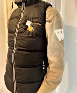 Gilet matelassé noir avec fermeture éclair, superposé sur un sweat-shirt beige.
