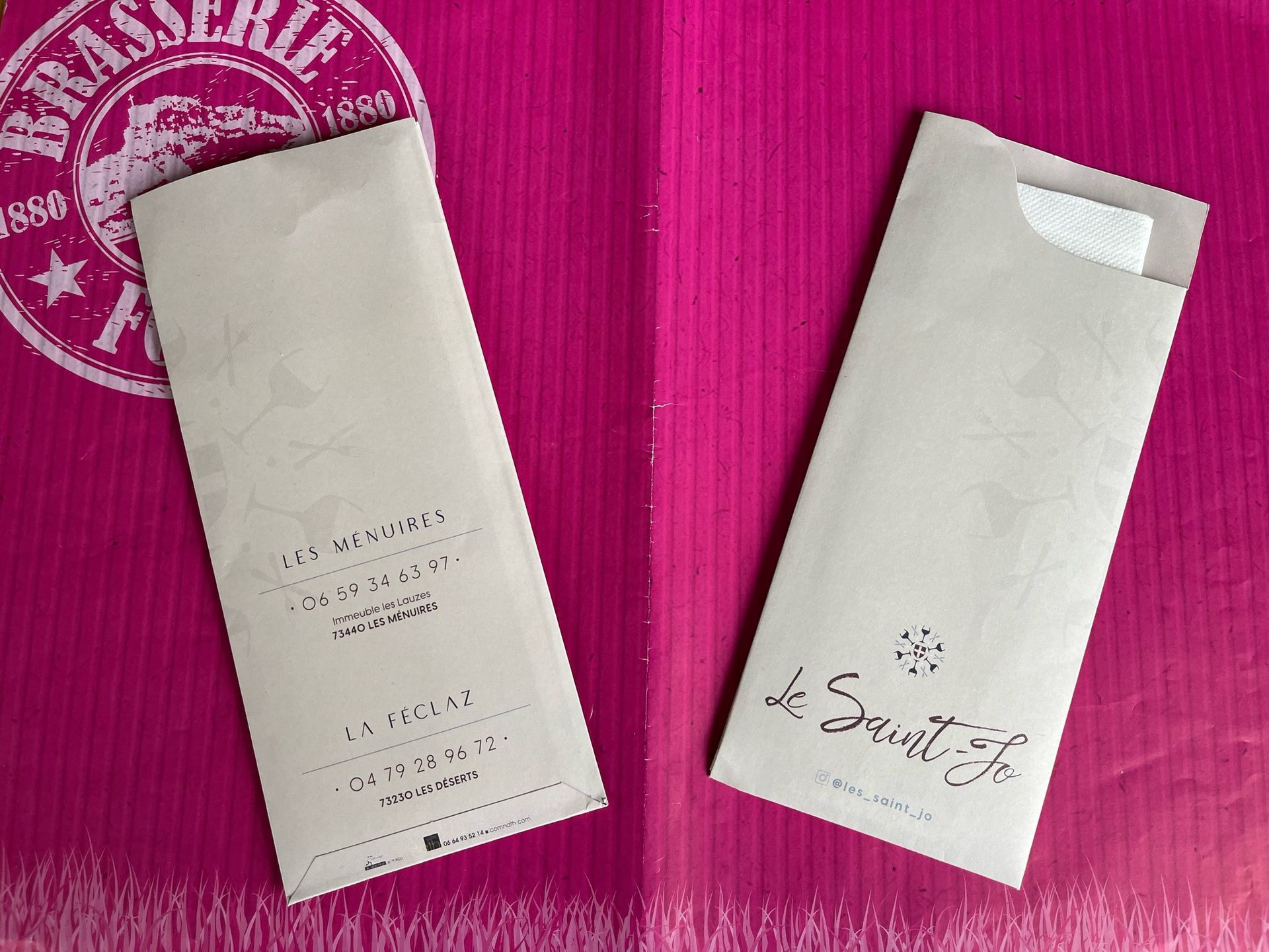 Deux pochettes en papier beige, l'une avec une serviette, sur fond rose. Texte et logo imprimés dessus.