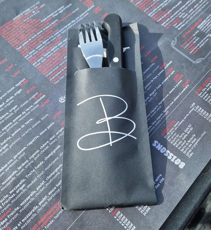Pochette à couverts noire avec une fourchette et un couteau, sur une table avec un menu imprimé.