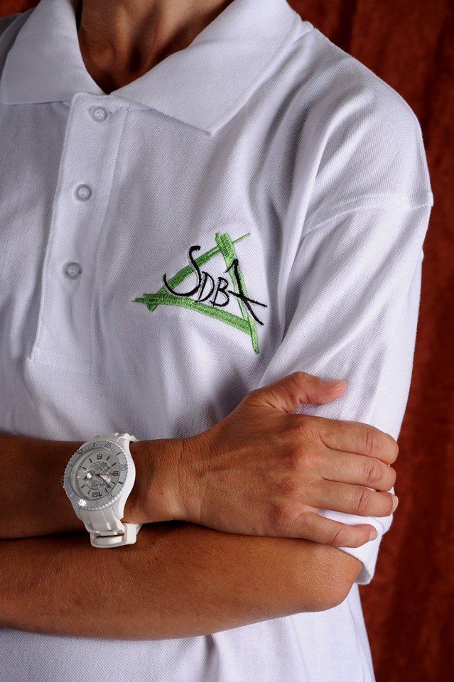 Personne en polo blanc avec logo, bras croisés, portant une montre blanche.
