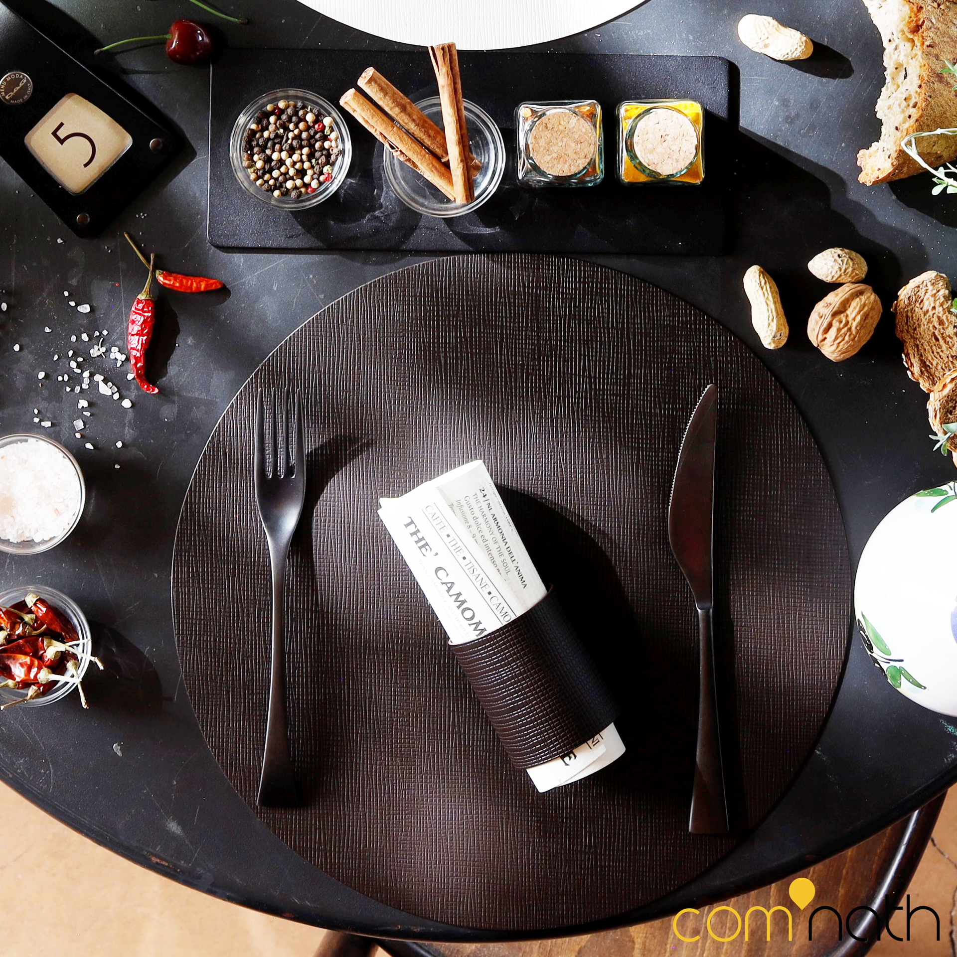 Décoration de table avec assiette, ustensiles, épices, cacahuètes et un rouleau de papier avec texte.