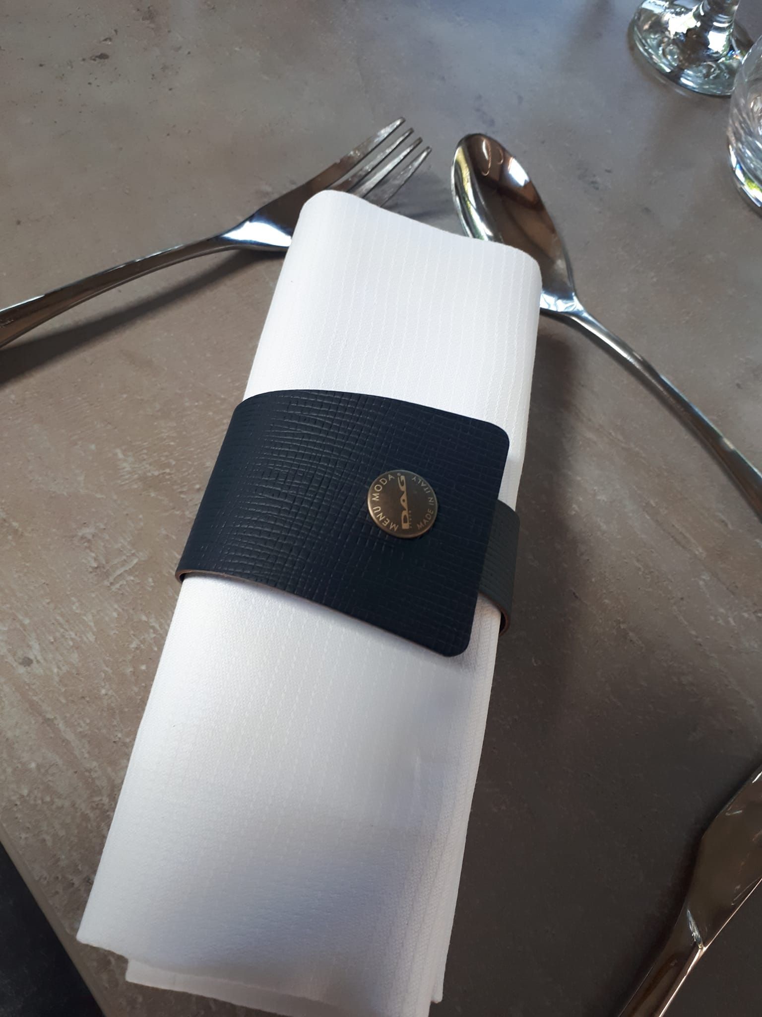 Serviette enveloppée dans un support en cuir noir avec bouton doré, avec fourchette et cuillère sur une table.