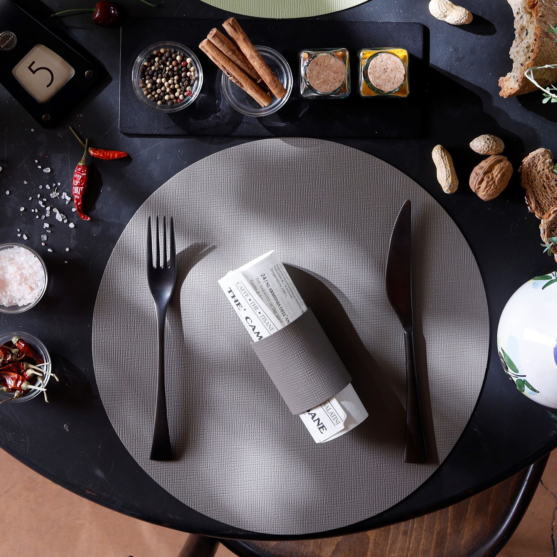 Couvert avec fourchette, couteau, serviette roulée et condiments sur un set de table rond.