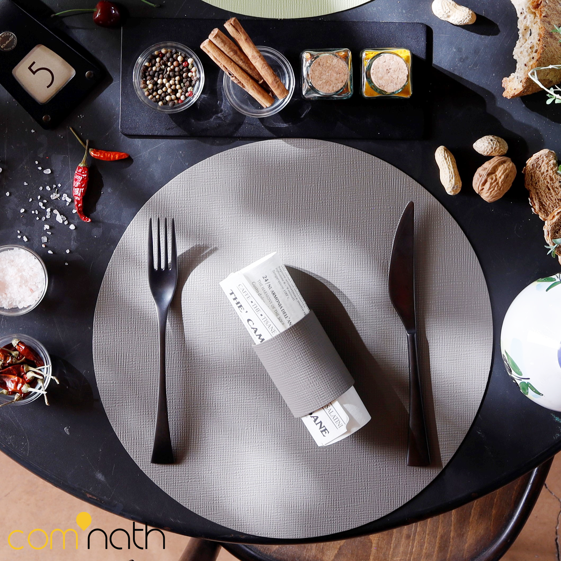 Couvert avec fourchette, couteau, serviette, assaisonnements et pain sur une table en bois foncé.