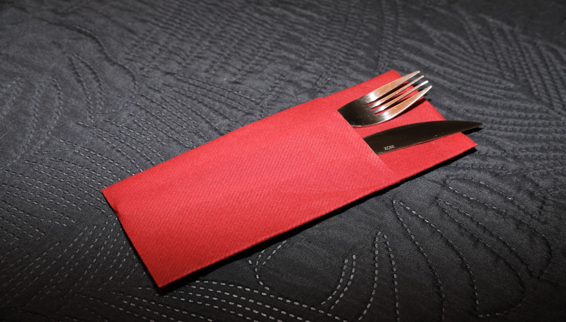 Serviette rouge avec fourchette et couteau sur une surface texturée sombre.