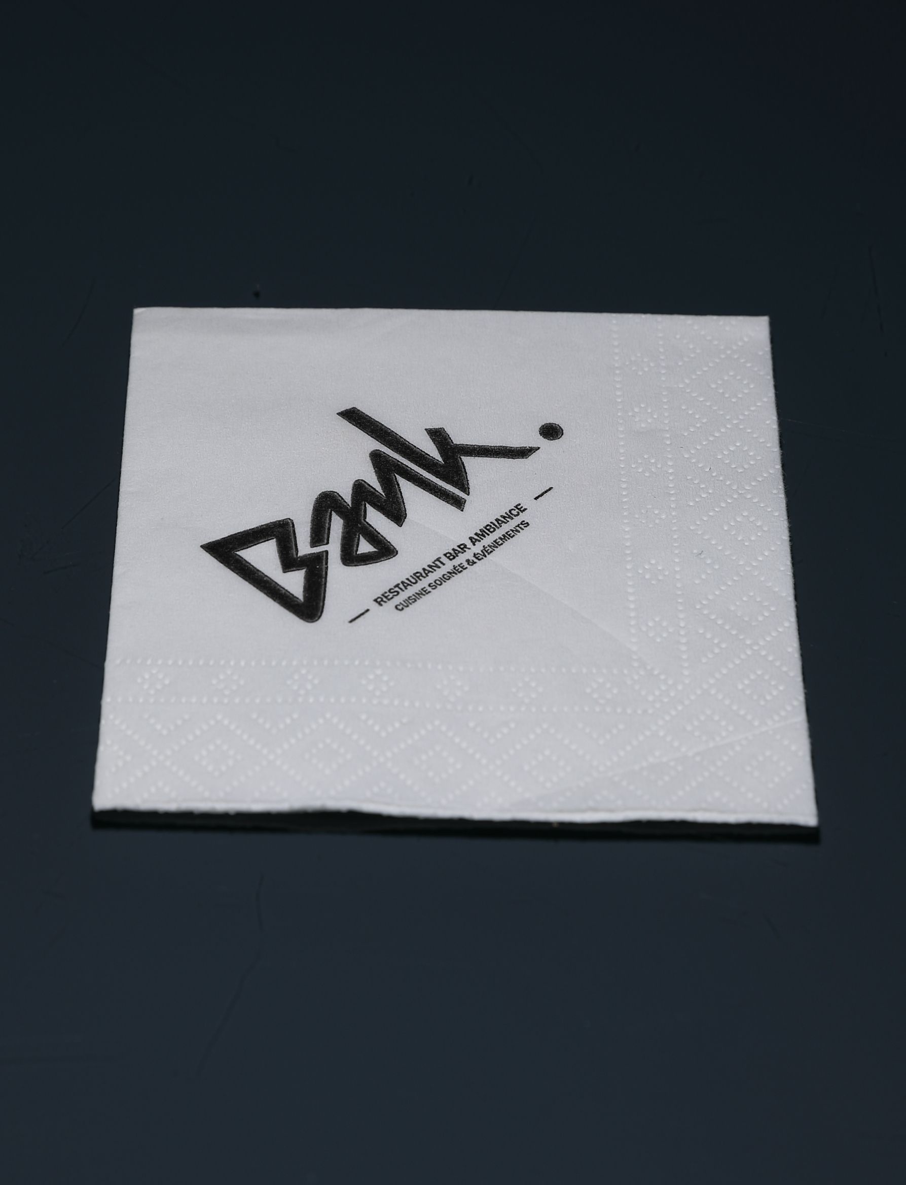 Serviette blanche avec logo noir « BMK » sur une surface sombre.