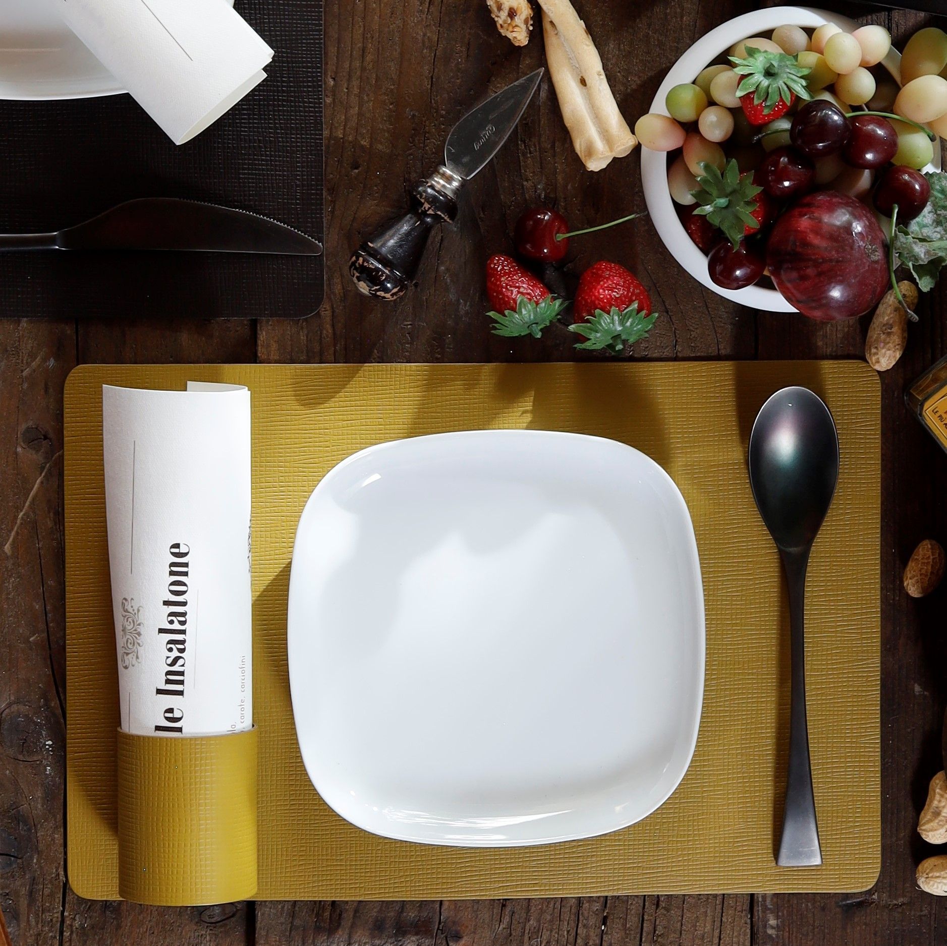 Une assiette blanche, une cuillère noire et une serviette roulée sur une planche à découper dorée posée sur une table en bois.