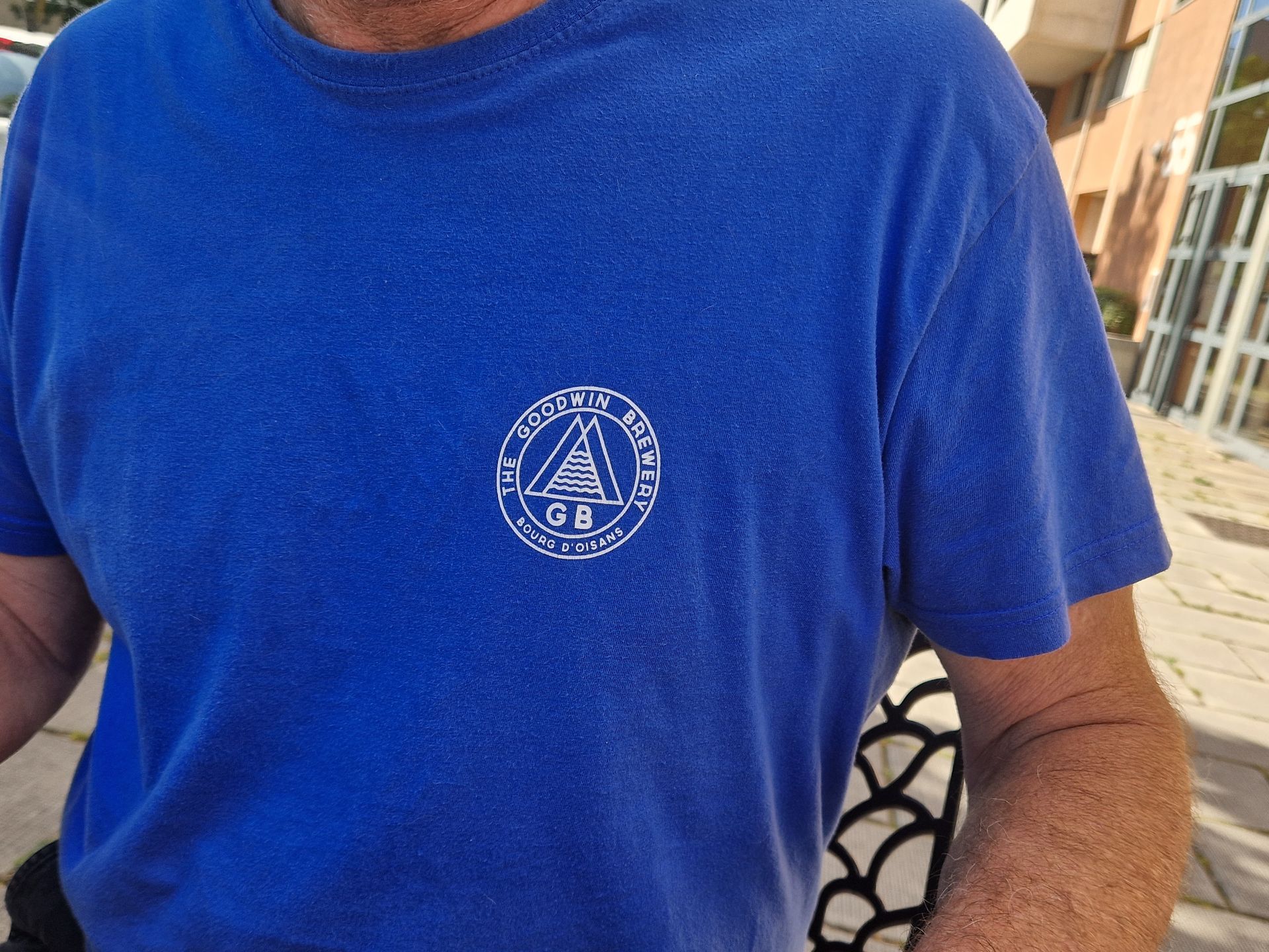 Homme portant un t-shirt bleu avec un logo circulaire blanc sur la poitrine.