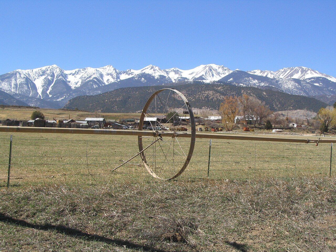 Farm field with a large irrigation wheel, mountains, and snow-capped peaks in the background.