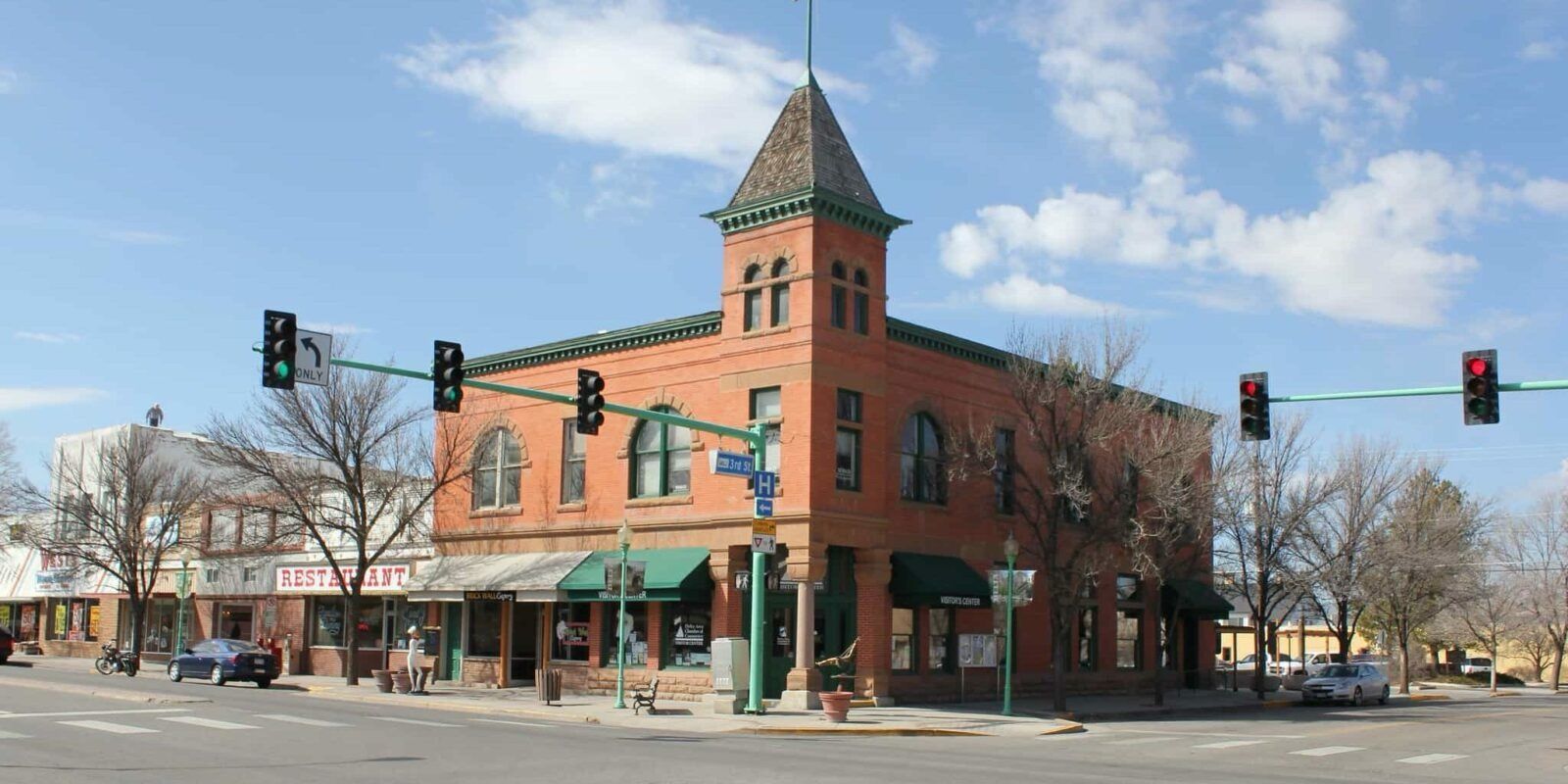 Street corner with a red brick historic building, green awnings, and traffic lights under a blue sky