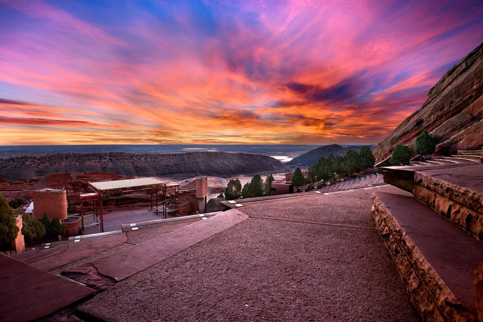 Sunset over a canyon overlook with a gravel path, stone wall, and vivid orange-purple sky