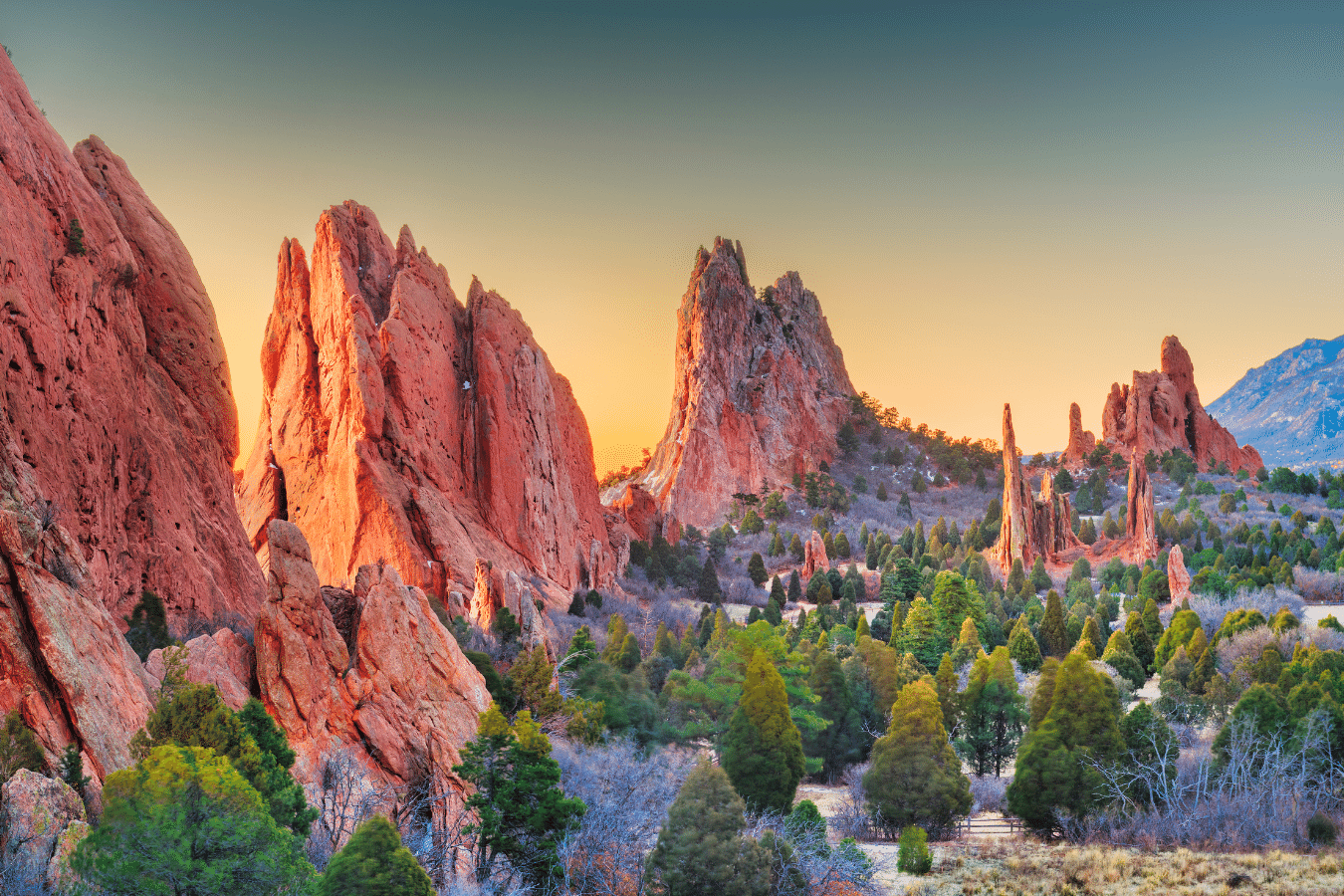 Sunset over red sandstone spires and green trees in a rocky desert landscape