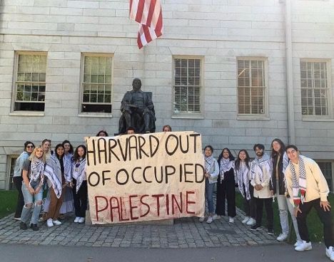 Students hold a banner reading “HARVARD OUT OF OCCUPIED PALESTINE” in front of a building.
