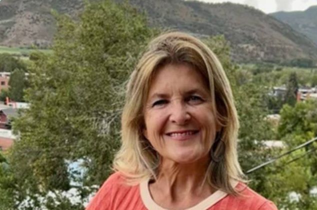 Smiling woman in a coral top with mountains and trees in the background