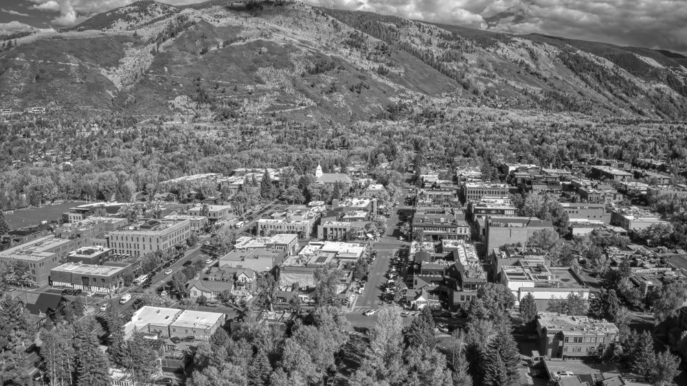 Aerial view of a small town nestled among trees with mountains in the background.