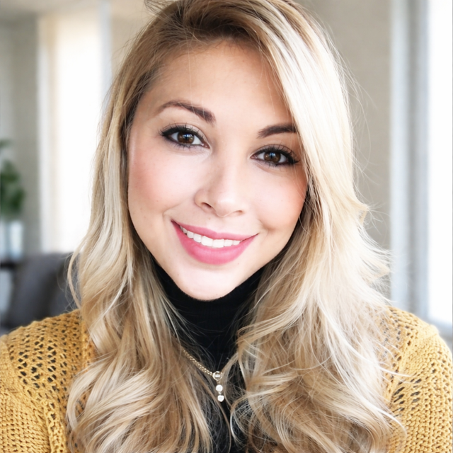 Smiling blonde woman in a black turtleneck and mustard sweater, facing the camera.