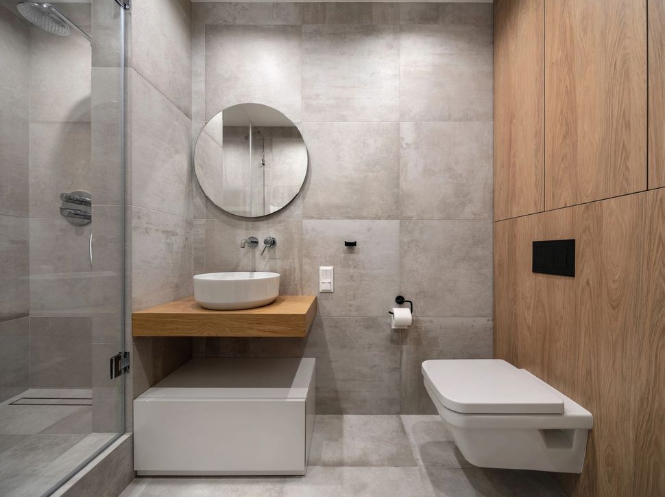 Bagno moderno e minimalista con piastrelle in pietra, dettagli in legno, lavabo sospeso, specchio e WC
