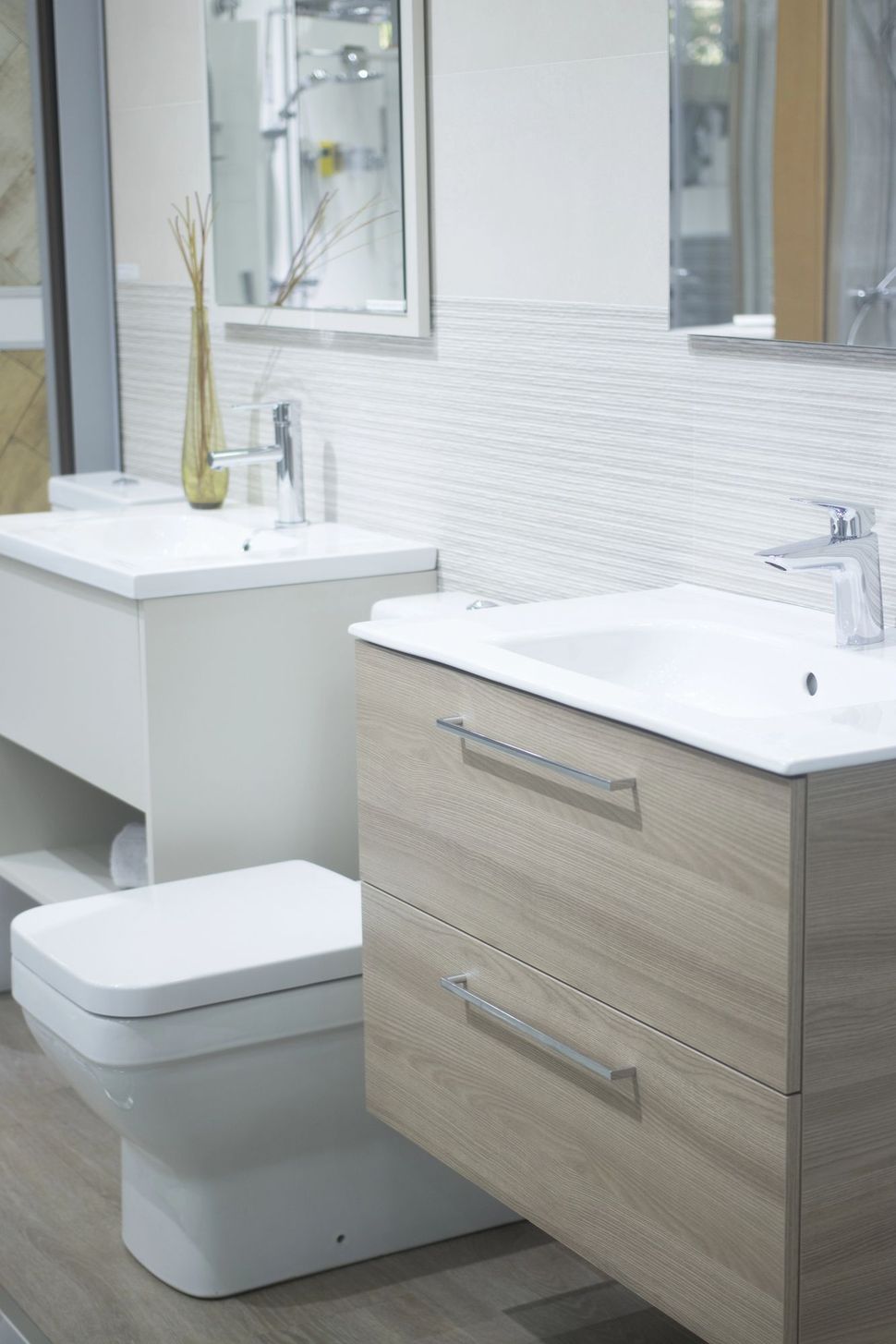 Bagno moderno con due lavandini, mobile lavabo in legno chiaro e WC sospeso sotto uno specchio.
