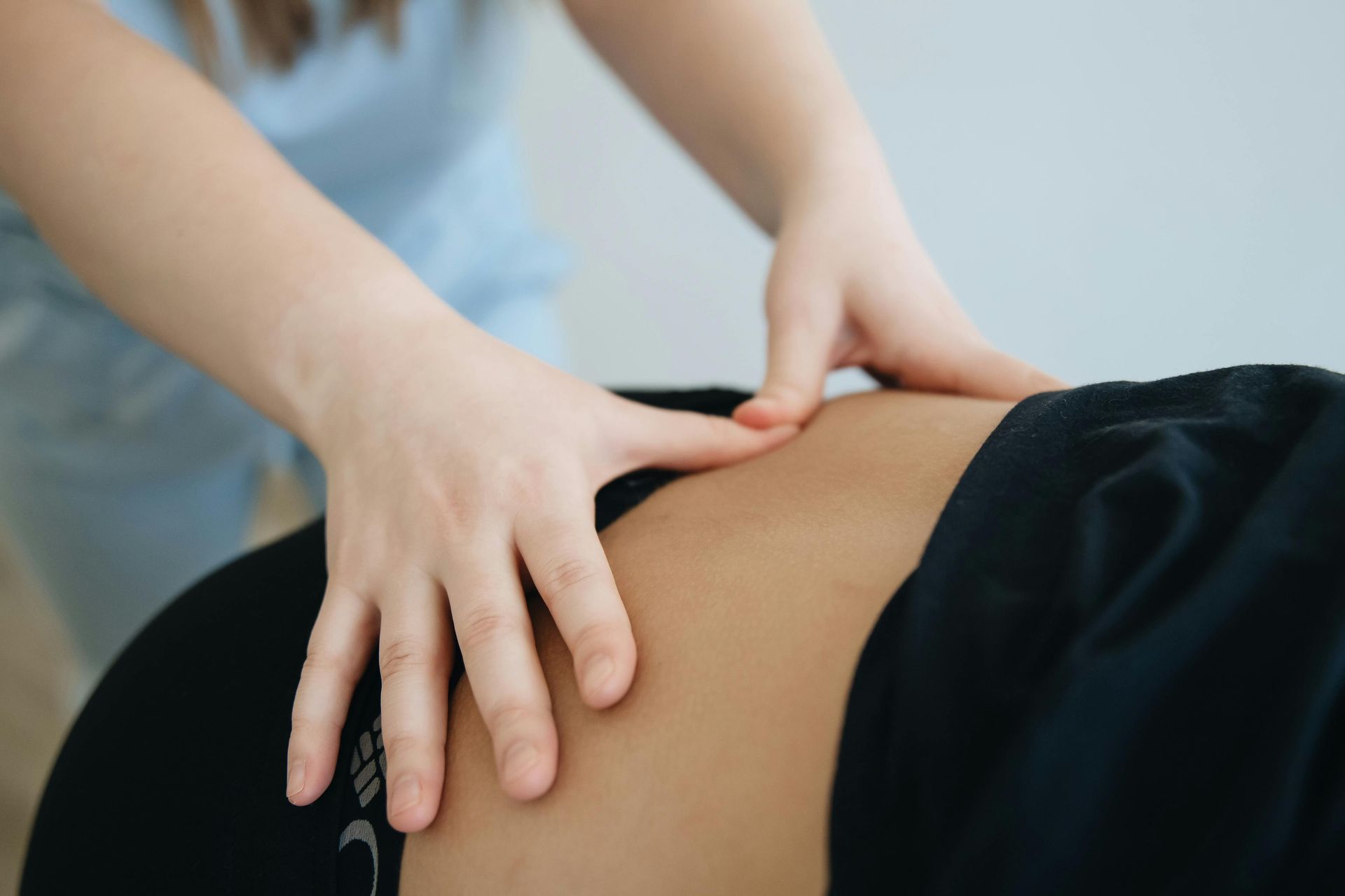 De handen van een therapeut voeren een zachte massage of fysiotherapietechniek uit op het heupgebied van een persoon.
