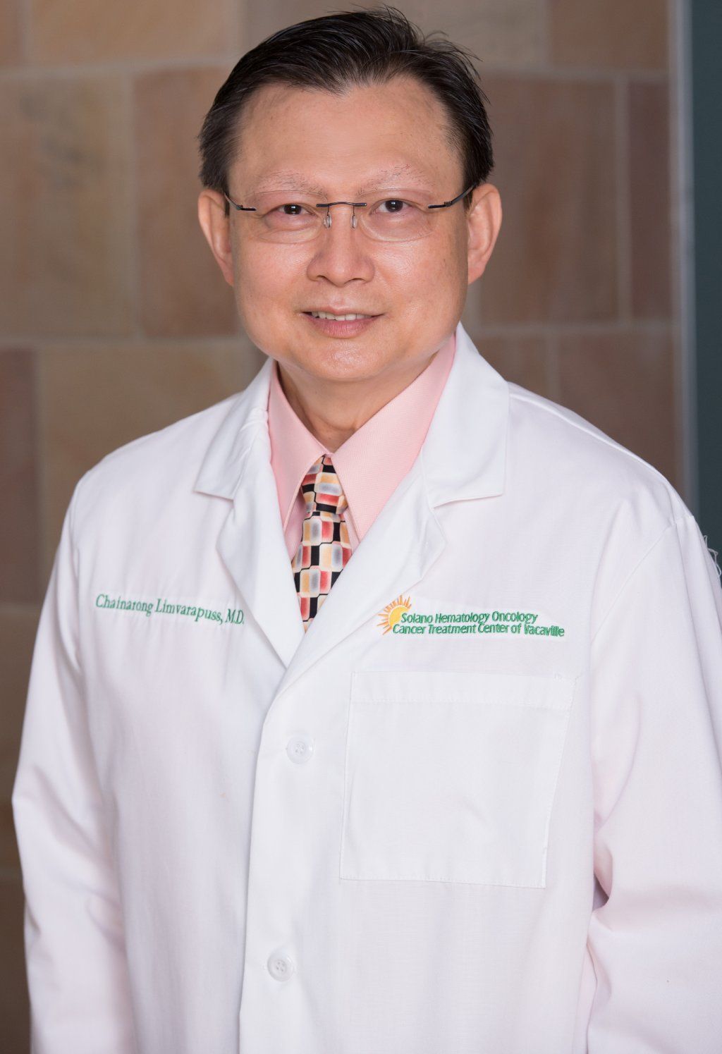 Chainarong Limvarapuss, M.D. in a white coat and tie is standing in front of a brick wall.