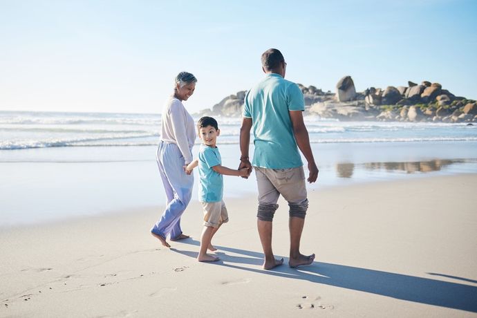 A family is walking on the beach holding hands.