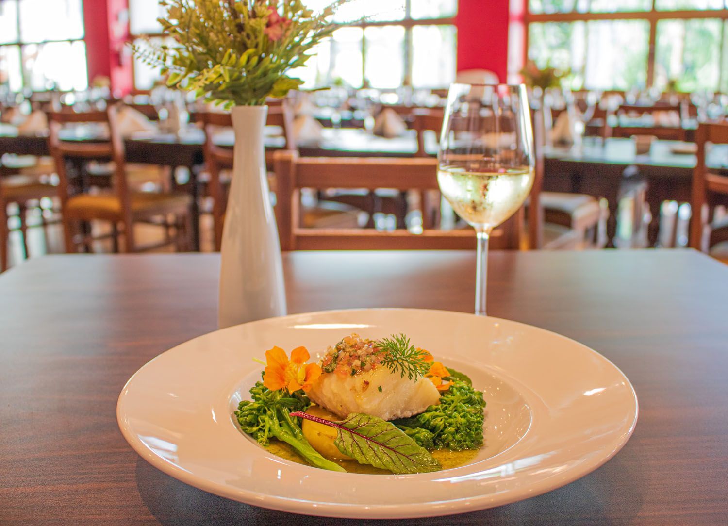 Prato de peixe com legumes e vinho branco em ambiente de restaurante.