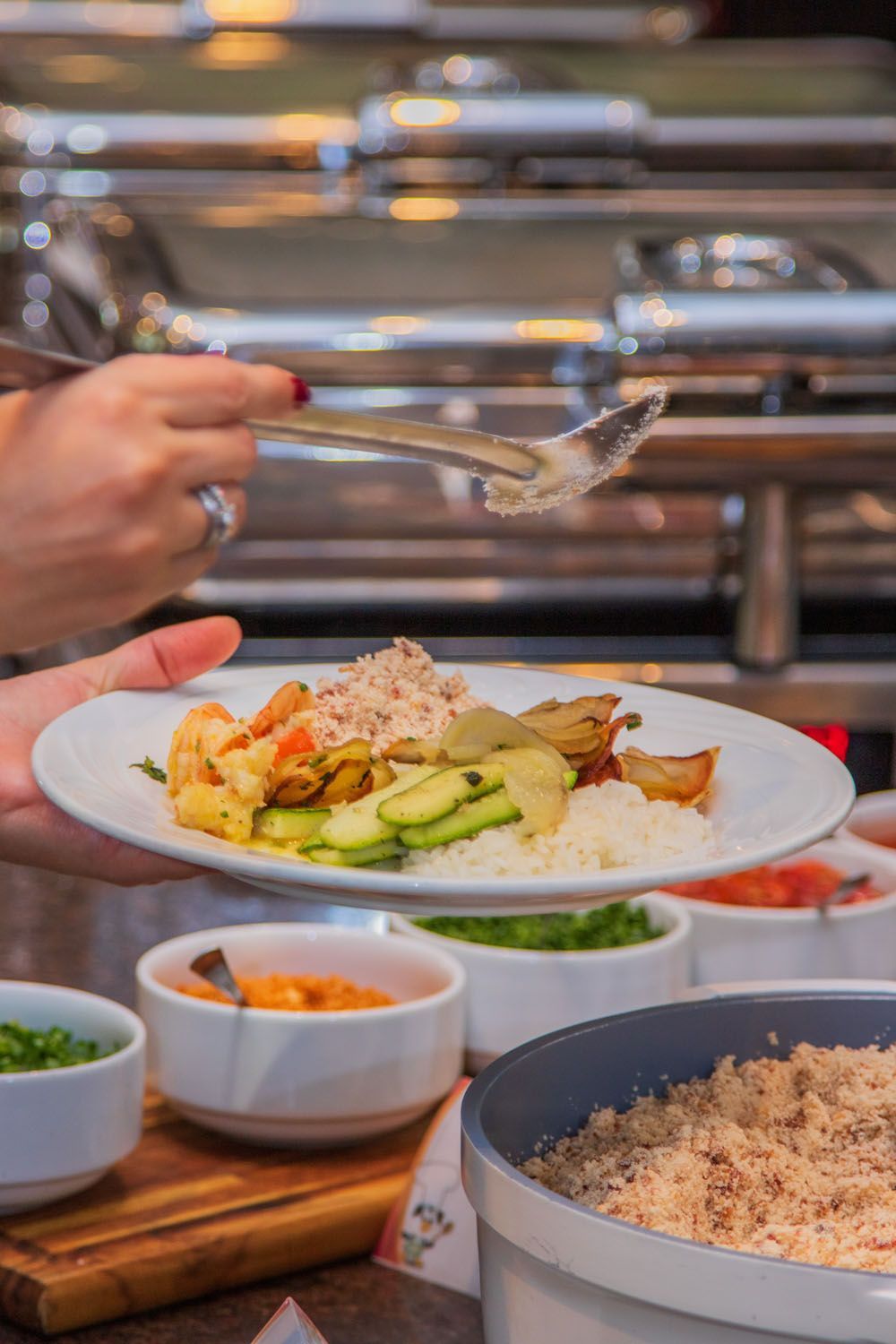 Pessoa servindo comida de um bufê. Prato com camarão, legumes e arroz.