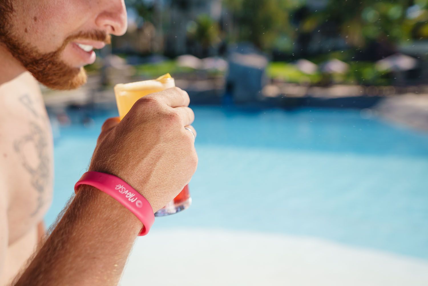Homem bebendo um coquetel na piscina; usando uma pulseira rosa.