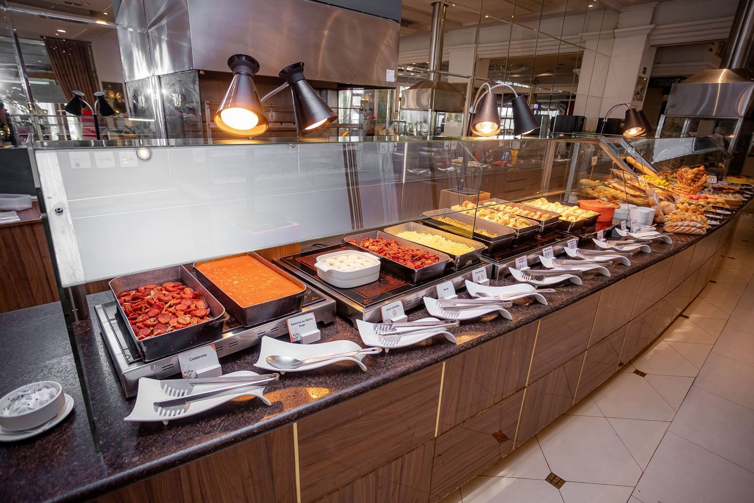 Buffet com pratos variados em um restaurante, incluindo saladas, pratos quentes e pães.