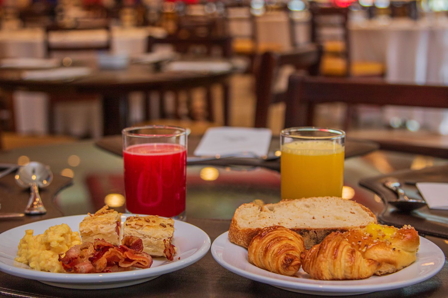 Café da manhã: pratos de comida, dois sucos e talheres em uma mesa em um restaurante.